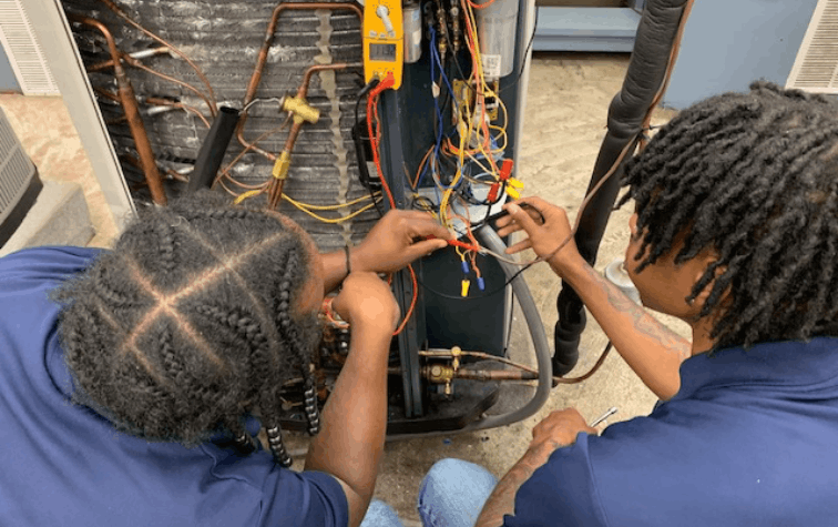 Two HVAC students working on an A/C system