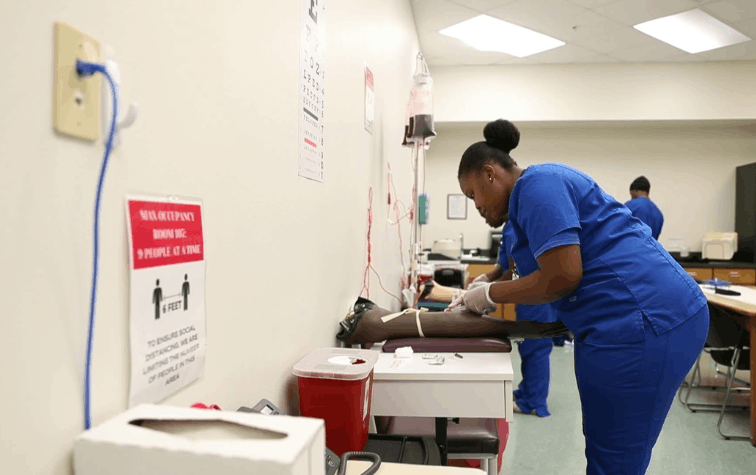 Medical Assistant student leaned over dummy arm, inserting IV